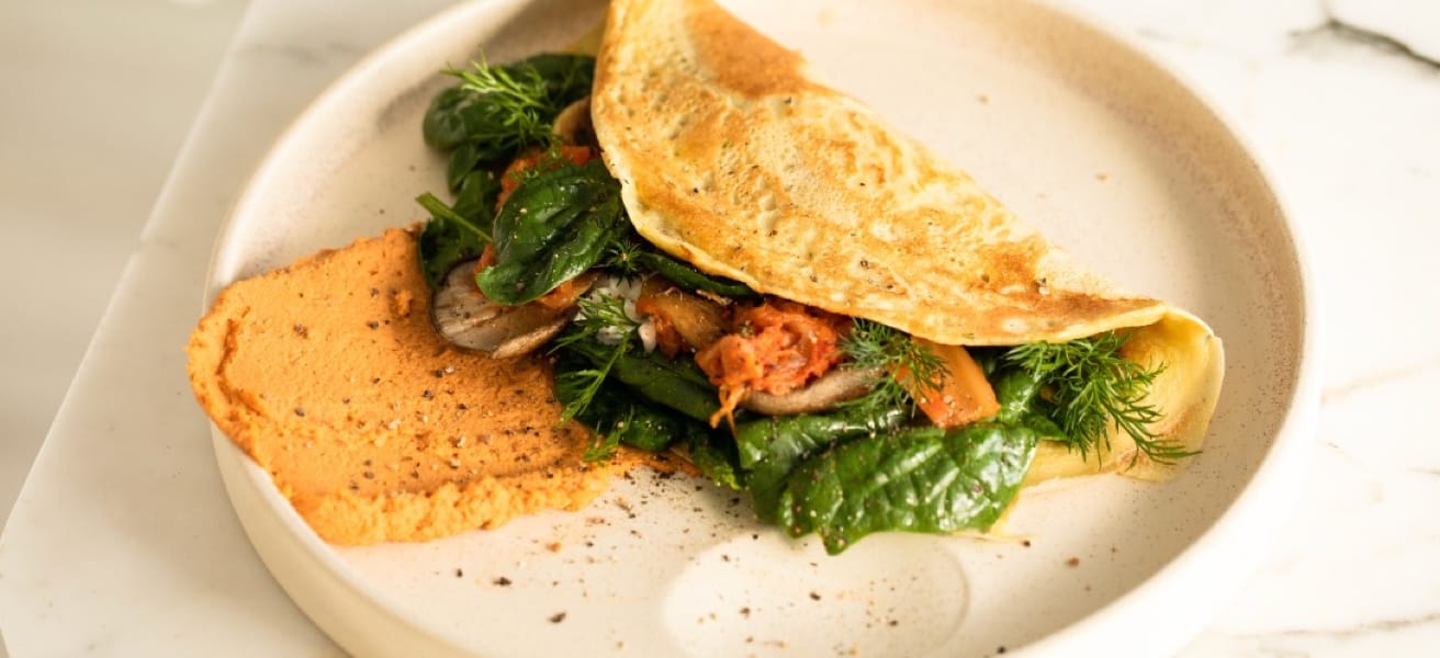 An omelette on a white plate, filled with various herbs and vegetables.